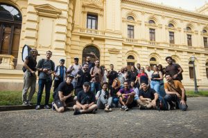 A diverse group of photographers gathered outside a historic building on a sunny day.